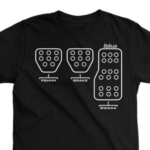 Peut inclure: T-shirt noir avec un graphique blanc de trois pédales de voiture étiquetées "PSHHH", "FREIN" et "BWAAA".