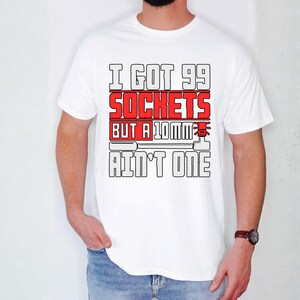 May include: White t-shirt with the text "I GOT 99 SOCKETS BUT A 10MM AIN'T ONE" in a bold, red and black design. The shirt is a classic crew neck style.