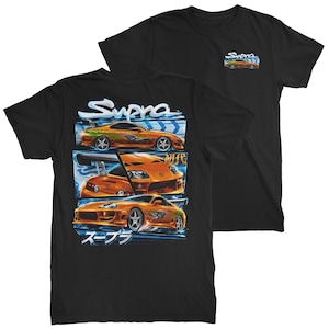 May include: A black t-shirt featuring a graphic print of an orange sports car. The back design displays three panels of the car with the text Supra and Japanese characters. The front chest area includes a smaller version of the orange car graphic.