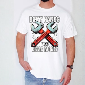 May include: White t-shirt featuring a graphic of two crossed wrenches in red and blue, with the text "DIRTY HANDS MAKE CLEAN MONEY" in a bold, blocky font. The design includes gear-shaped elements.