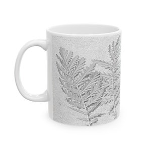 May include: White ceramic mug featuring a grey fern design. The fern is a delicate, intricate pattern that covers the entire mug.