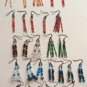 May include: A collection of beaded earrings in various colors and designs. Styles include dangling, fringed, and linear arrangements. Colors range from black and white to vibrant blues, oranges, and greens. The earrings are displayed on a white surface.