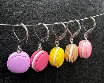 May include: Four pairs of earrings featuring miniature macarons in purple, pink, yellow, and brown colors.