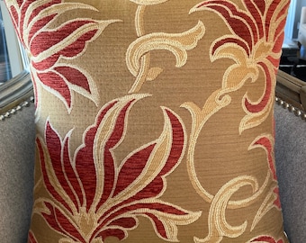 May include: A decorative throw pillow with a floral pattern in shades of gold and red. The pillow features a stylized floral design with intricate details.