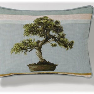 May include: A light blue throw pillow with a green bonsai tree embroidered on it. The pillow has a light blue background with a white and light blue stripe at the top and bottom.