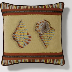 May include: A decorative pillow with a beige background and two seashells in the center. The seashells are yellow, blue, and brown with a striped pattern. The pillow has a brown border with multi-colored stripes.