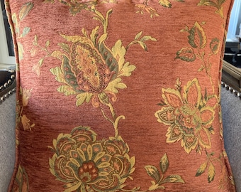 May include: A rust-colored throw pillow with a floral pattern in shades of green, yellow, and brown. The pillow has a textured fabric and a subtle sheen.