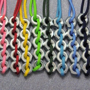 May include: A close-up of ten colorful braided necklaces made with nuts and string. The necklaces are in a rainbow of colors, including red, pink, yellow, green, blue, black, and purple.
