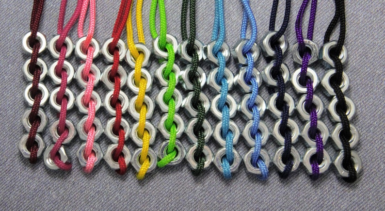 May include: A close-up of ten colorful braided necklaces made with nuts and string. The necklaces are in a rainbow of colors, including red, pink, yellow, green, blue, black, and purple.