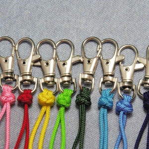 May include: A set of 12 colorful keychains with silver swivel clips. Each keychain has a different color cord with a knot at the top.