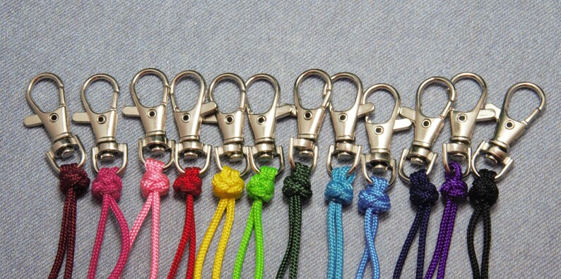 May include: A set of 12 colorful keychains with silver swivel clips. Each keychain has a different color cord with a knot at the top.