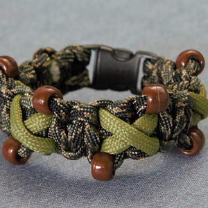 May include: A green and black camouflage paracord bracelet with brown plastic beads. The bracelet has a black plastic buckle.