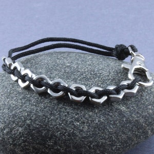 May include: A black paracord bracelet with a silver metal chain and a silver clasp. The bracelet is on a gray rock.