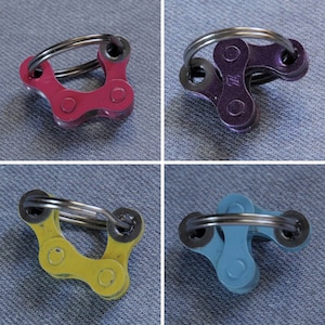 May include: Four different colored bike chain keychains. The keychains are made of metal bike chains and are in the colors pink, purple, yellow, and blue.