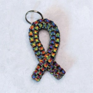May include: A colorful paracord keychain in the shape of a ribbon. The ribbon is made of blue, green, yellow, and red paracord. The keychain has a silver key ring.