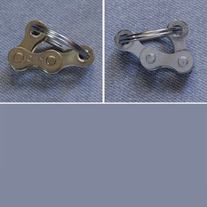 May include: Two silver bike chain keychains, one with a silver ring and the other with a gold ring. The keychain with the gold ring has the word "KMC" printed on it.