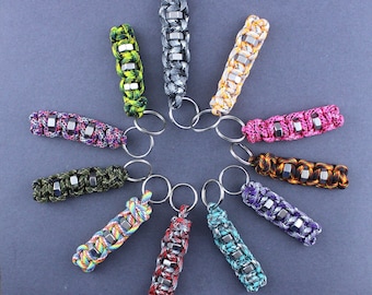 Puede incluir: Una colección de 11 llaveros coloridos con diferentes patrones y diseños. Cada llavero presenta una serie de cuentas hexagonales de metal y un anillo de llave plateado.