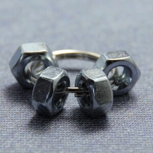 Puede incluir: Un anillo de metal plateado hecho de cuatro tuercas conectadas con un alambre.