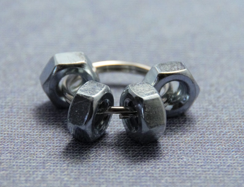 Puede incluir: Un anillo de metal plateado hecho de cuatro tuercas conectadas con un alambre.