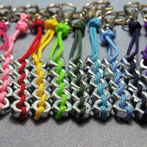 May include: A collection of colorful keychains made with nuts and string. The keychains are in various colors, including red, pink, yellow, green, blue, purple, and black.