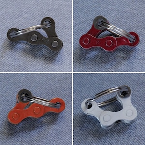 May include: Four different colored bike chain fidget toys. The toys are made of metal and have a ring on the top. The colors are black, red, orange, and silver.