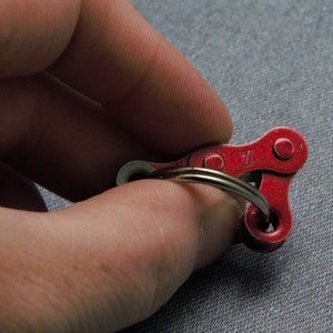 May include: A red metal keychain shaped like a bicycle chain link. The keychain has a silver ring attached to it.