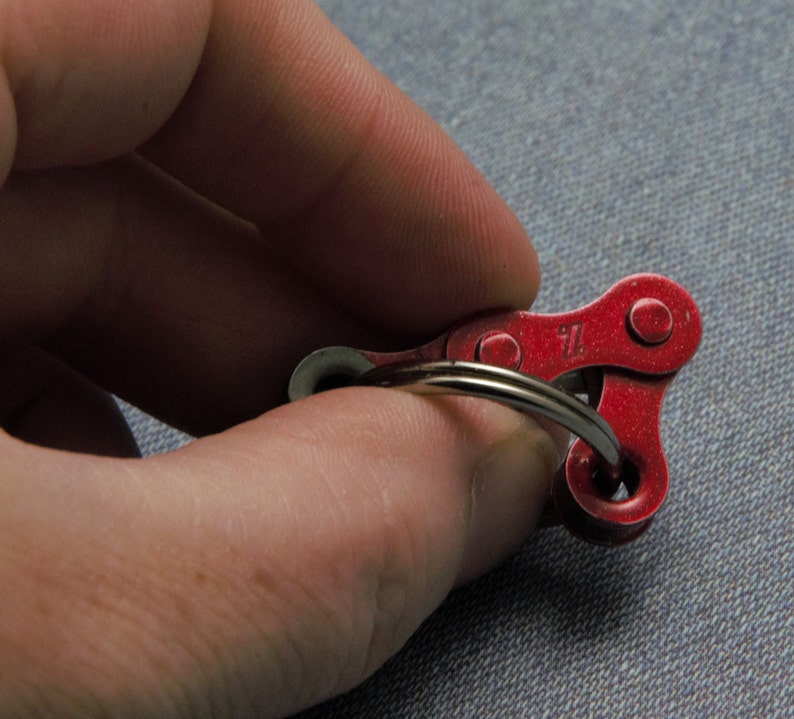 May include: A red metal keychain shaped like a bicycle chain link. The keychain has a silver ring attached to it.