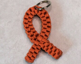 May include: A brown paracord keychain in the shape of a ribbon. The keychain has a silver metal ring.