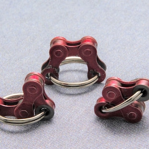 May include: Three red metal fidget toys made from bike chain links. Each toy has a silver ring in the center.