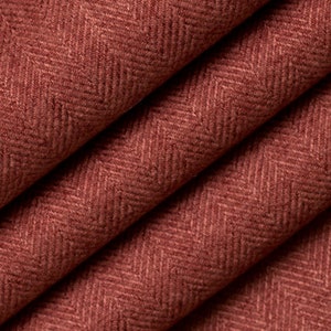May include: Close-up of a folded fabric with a herringbone pattern. The fabric is a warm, reddish-brown color, with the diagonal weave creating a textured appearance. The folds add depth and dimension to the textile.