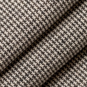 May include: Close-up of a black and white houndstooth fabric. The fabric has a woven texture and a subtle sheen.