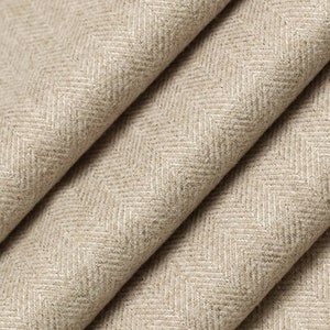 May include: Close-up of a beige herringbone fabric with a subtle texture. The fabric is folded in a way that shows the pattern and weave.