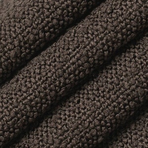 Può includere: Primo piano di un tessuto marrone scuro con una superficie strutturata e ad anello. Il tessuto è piegato, creando linee diagonali e ombre. Il materiale appare morbido e felpato, adatto all'abbigliamento o all'arredamento.