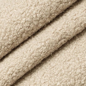 May include: Close-up of a soft, beige fabric with a textured, curly surface. The fabric has a fuzzy, plush appearance.