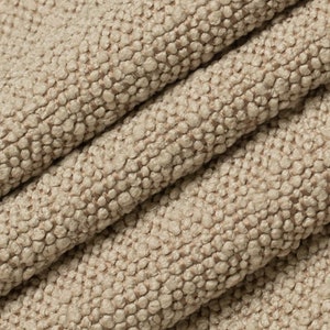 Può includere: Primo piano di un tessuto beige testurizzato con un motivo intrecciato. Il tessuto ha una texture morbida e soffice.