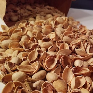 May include: A pile of light brown pistachio shells. The shells are empty and have a slightly rough texture.