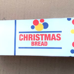 May include: Rectangular box with the words "CHRISTMAS BREAD" in red letters. The box has a light blue background with red, yellow, and blue polka dots. Blue lines frame the text.