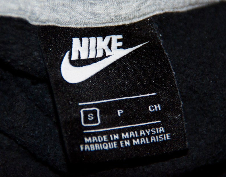 May include: Black and white Nike logo tag with the text "NIKE" in white. The tag also includes the size "S", "P", and "CH" in white. The tag reads "Made in Malaysia" and "Fabrique en Malaisie" in white.