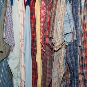 May include: A collection of plaid shirts in various colours, including red, blue, green, and yellow. The shirts are hanging on a rack and are all made of cotton.