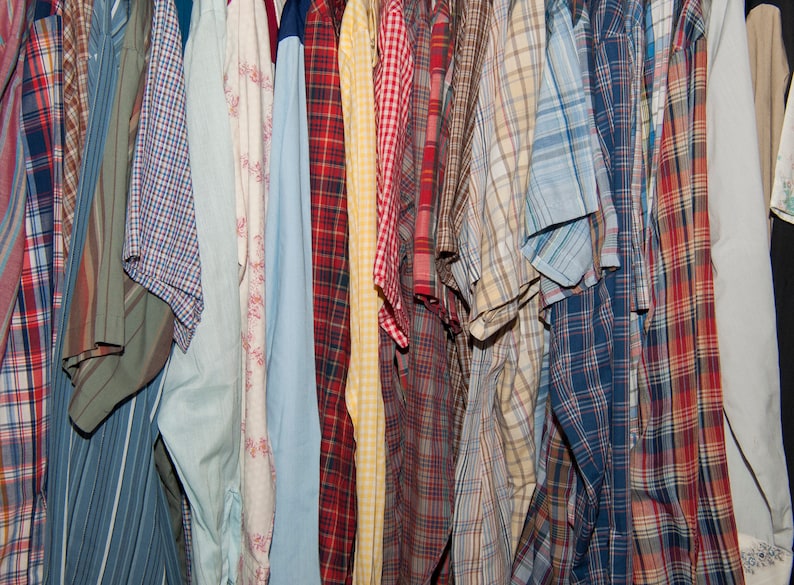 May include: A collection of plaid shirts in various colours, including red, blue, green, and yellow. The shirts are hanging on a rack and are all made of cotton.