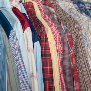 May include: A collection of plaid shirts in various colours and patterns, including red, blue, yellow, and brown. The shirts are hanging on a rack and are all made of a soft, comfortable fabric.