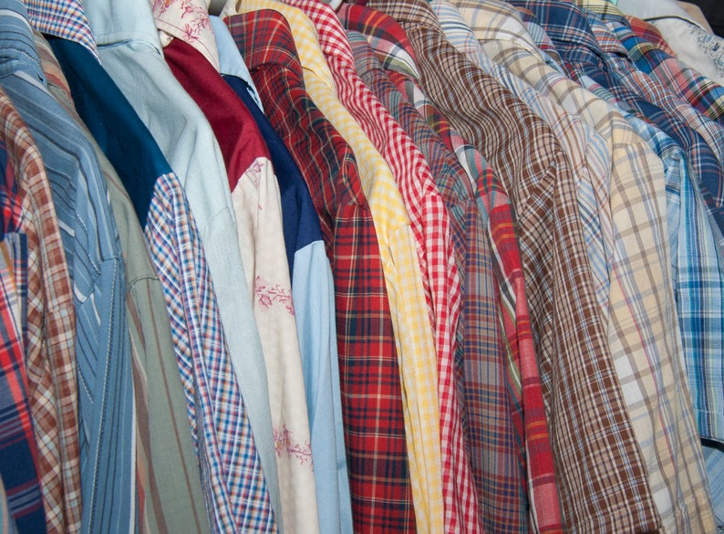 May include: A collection of plaid shirts in various colours and patterns, including red, blue, yellow, and brown. The shirts are hanging on a rack and are all made of a soft, comfortable fabric.