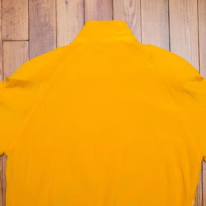 以下が含まれることがあります： ハイカラーとジッパーが付いた明るい黄色のジャケット。 ジャケットはシンプルなデザインで、滑らかな質感です。 袖は短く、全体的なスタイルはカジュアルです。