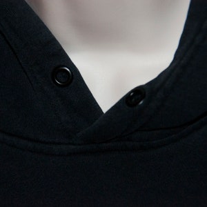 May include: Close-up of a black hooded sweatshirt with two black buttons on the neckline.