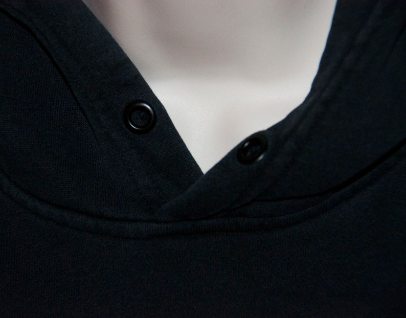 May include: Close-up of a black hooded sweatshirt with two black buttons on the neckline.