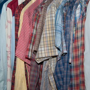 May include: A collection of plaid shirts in various colours, including blue, red, yellow, and green. The shirts are hanging on a rack and are all button-down.