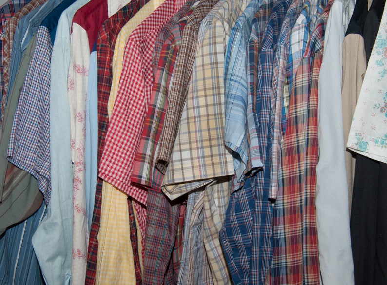 May include: A collection of plaid shirts in various colours, including blue, red, yellow, and green. The shirts are hanging on a rack and are all button-down.