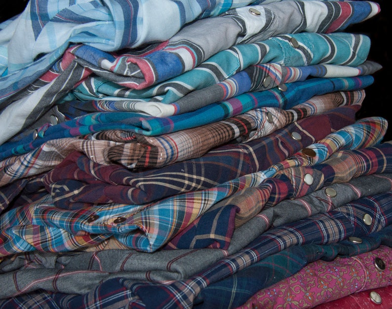 May include: A stack of plaid and striped shirts in various shades of blue, red, and brown. The shirts are folded and stacked on top of each other, creating a layered effect.