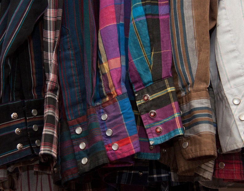 May include: A collection of plaid shirts in various colours, including blue, purple, red, and brown. The shirts are all button-down and have a casual style.