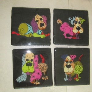 May include: Set of four black square coasters with colorful cartoon dogs on each. The dogs are wearing different patterned clothes and have different facial expressions.